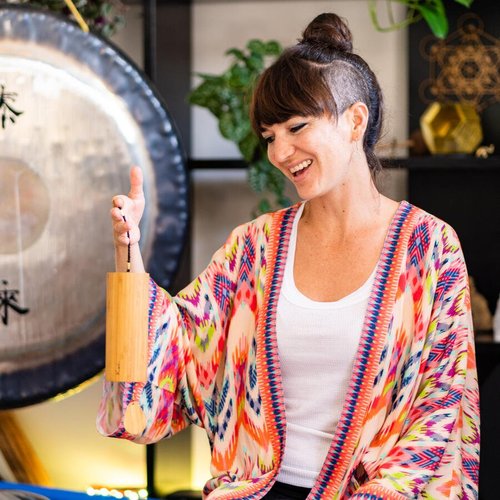 Woman smiling, wearing colorful kimono, holding a wooden wind chime, with a gong in the background.